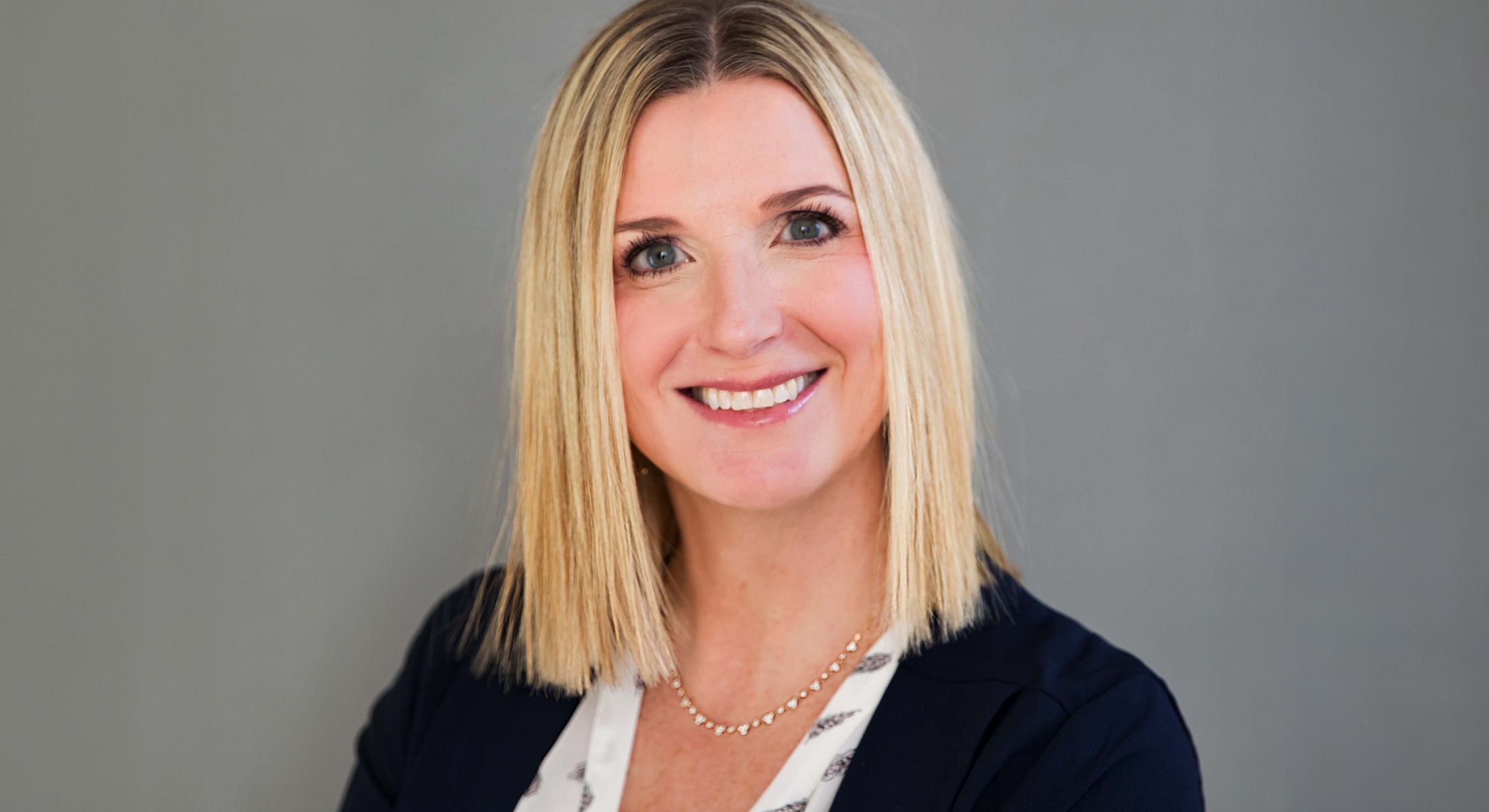 Smiling woman with blonde hair and necklace.