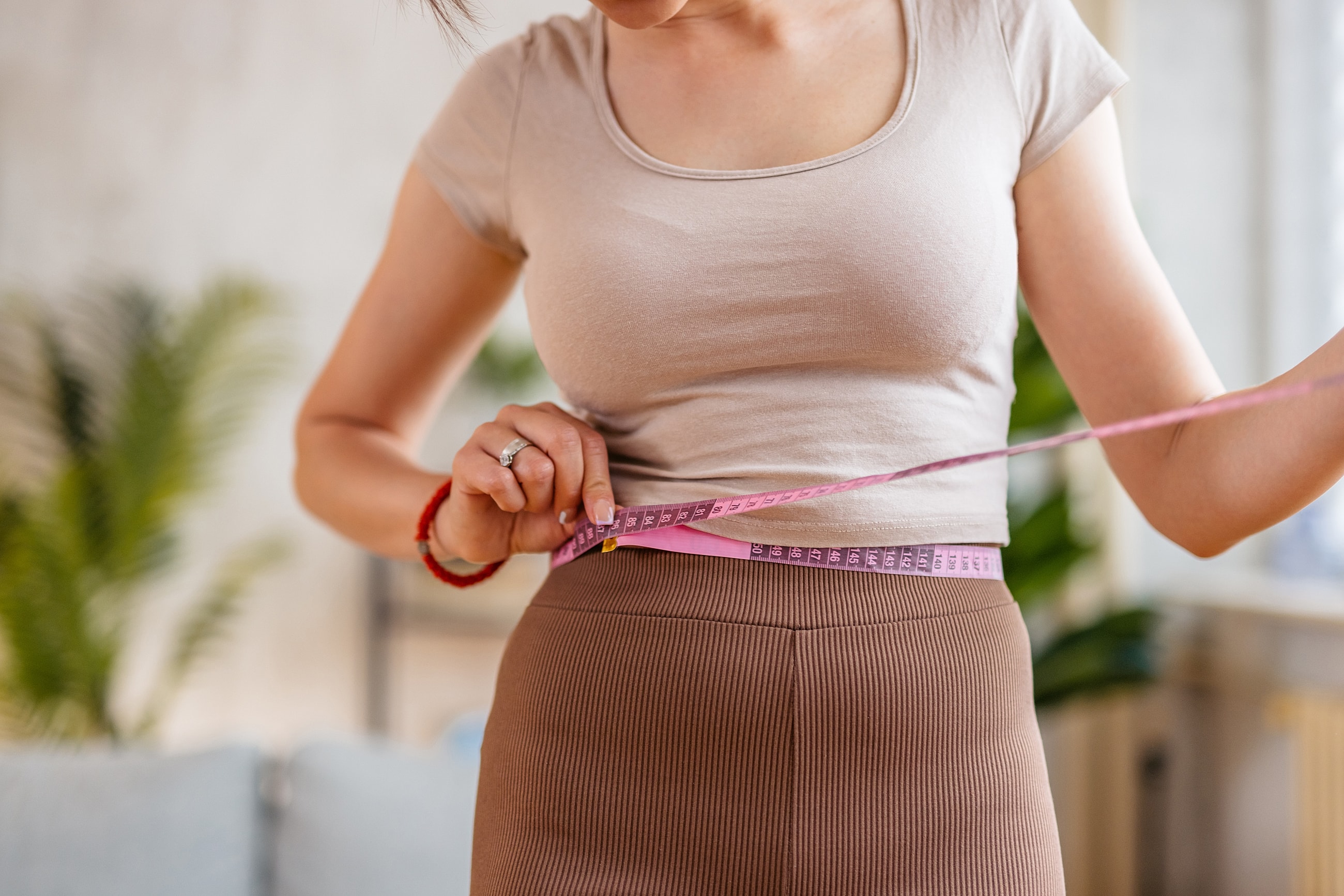 Measuring waist with a tape measure indoors.