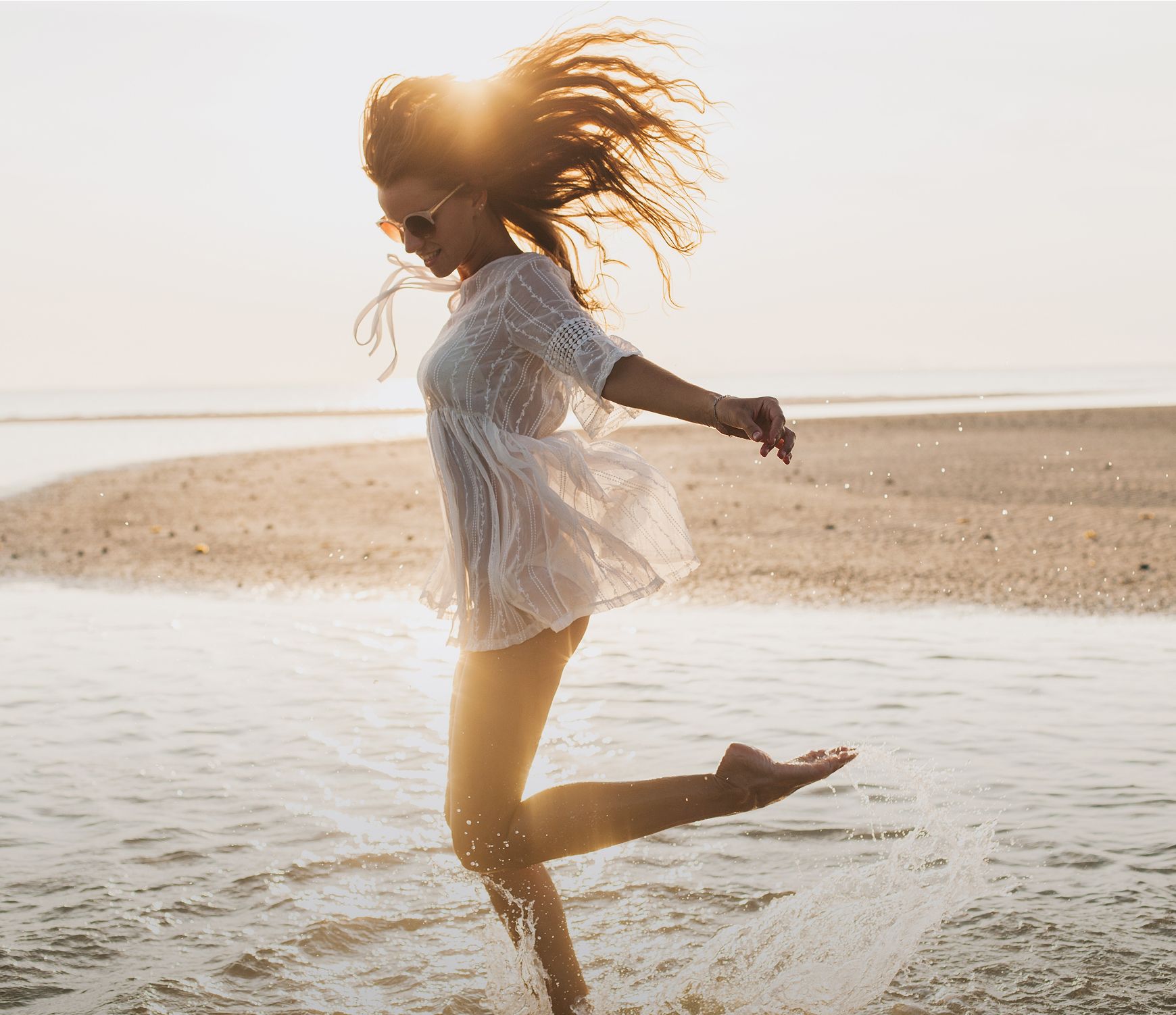 Woman splashing in shallow water at sunset.