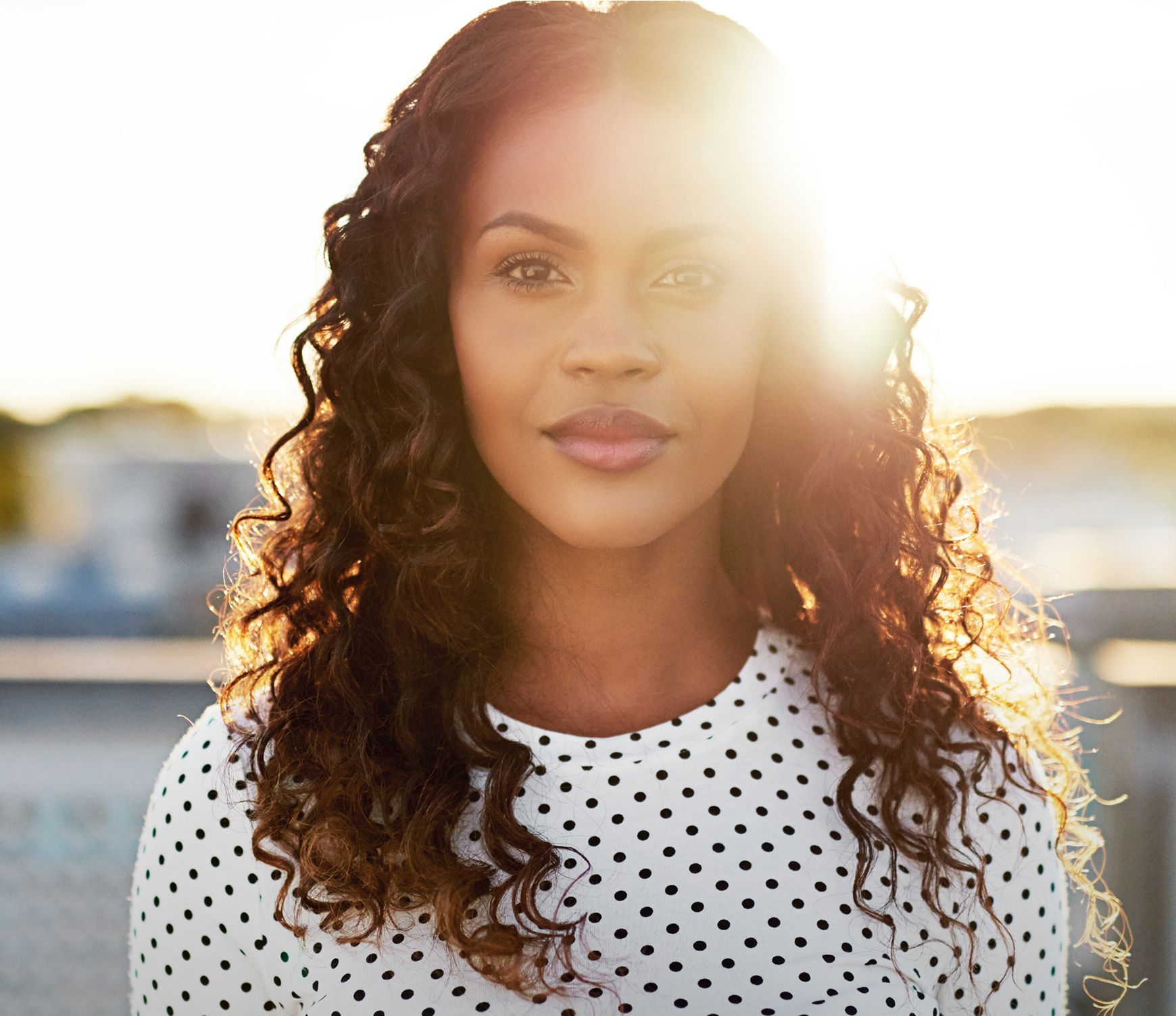 Woman with curly hair in sunlight, polka dot shirt.